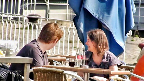 Redhead guy and brunette woman smiling intimately at outdoor cafe table with drinks