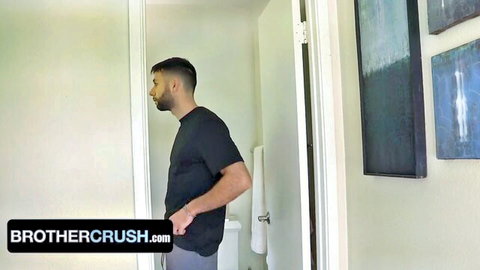 Muscular bearded stepbrother in tight gray pants stands sideways in bathroom doorway on BrotherCrush