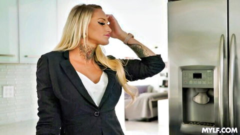 Curvy blonde MILF with big tits and neck tattoo touching head in kitchen by fridge