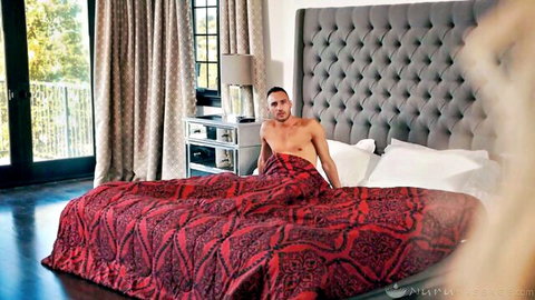 Muscular shirtless hunk lounging on red luxury bed wrapped in towel teasing cock bulge