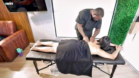 Black masseur rubbing hands on nude Asian woman's bare oiled back during erotic massage