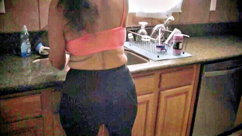 Laney Grey in pink crop top and black leggings, bending over kitchen sink