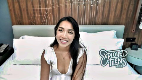 Petite Latina teen smiling in low-cut white dress, teasing cleavage