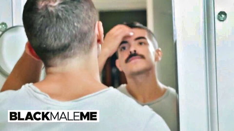 Man with mustache grooms eyebrow in bathroom mirror reflection while viewed from behind