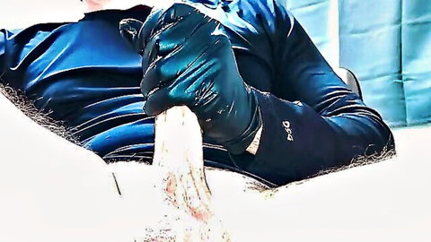 Man in black latex gloves gripping thick white dildo tightly on bed
