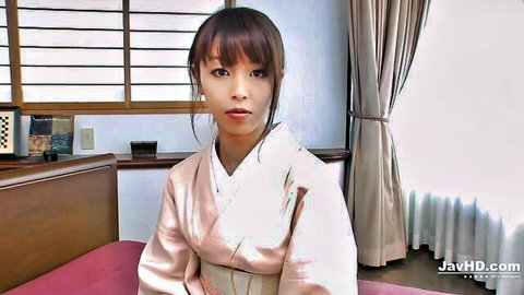 Cute Asian teen in pink kimono sitting on bed in Japanese room teasing