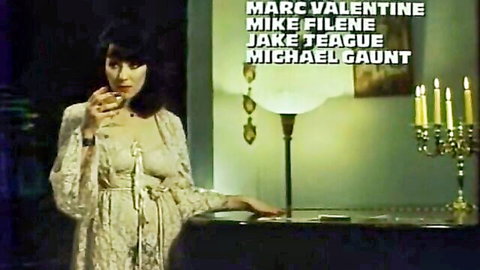 Seductive brunette in sheer lace robe smoking cigarette by candlelit desk in vintage adult film