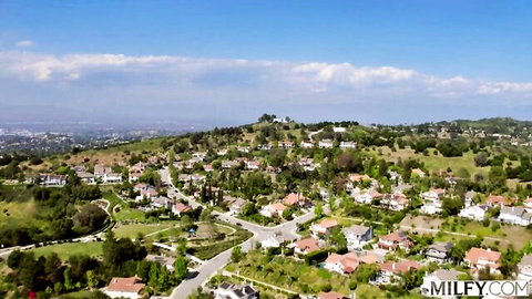 Aerial drone view of suburban hillside neighborhood with red-roofed houses and green hills