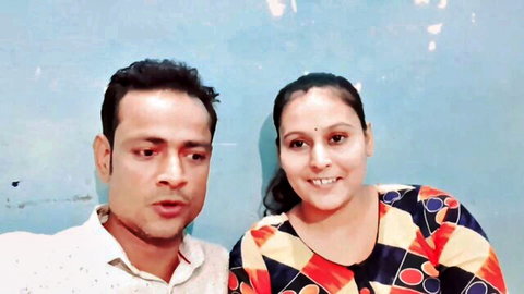 Smiling South Asian Indian couple posing together fully clothed against blue wall