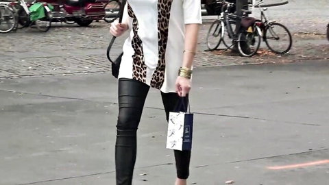 Sexy babe in tight black leather pants and leopard print top posing confidently on urban street