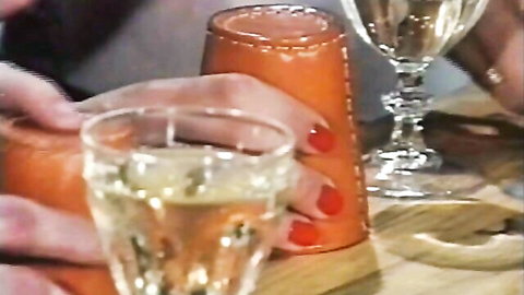 Close-up of feminine hands with red nails holding orange tumbler and champagne glass on wooden table
