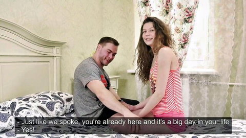 Nervous curly-haired amateur teen in pink striped tank top holds hands with guy on bed during first-time casting interview
