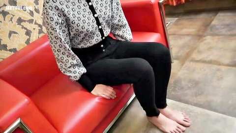 Asian woman in buttoned blouse and tight pants, sitting barefoot teasingly