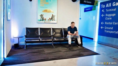 Man sits alone on chairs in brightly lit airport terminal with Brazzers watermark