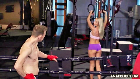 Skinny blonde with long hair and bubble butt in tight purple shorts poses in gym for shirtless boxer dude