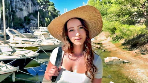 Brunette in white low-cut dress and hat, holding knife on sunny yacht marina, teasing cleavage