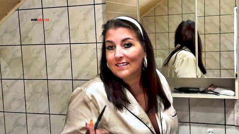 Busty MILF smiling in open satin robe flashing deep cleavage big tits applying makeup in bathroom mirror