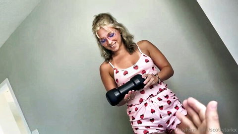 Venus Rivers teases in pink strawberry romper holding black dildo, smiling POV