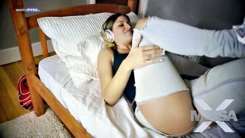 Skinny brunette teen with headphones bends over bed, ripped jeans down exposing shaved pussy and ass in POV doggy pose