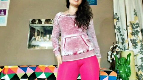 Sexy curly-haired woman in tight pink leggings and dusty rose hoodie posing confidently with hands in pockets