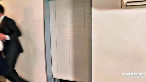 Blurry suited Japanese man walking in room with blinds and AC unit