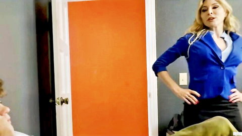 Blonde MILF in tight blue blazer and skirt poses seductively hands on hips by door