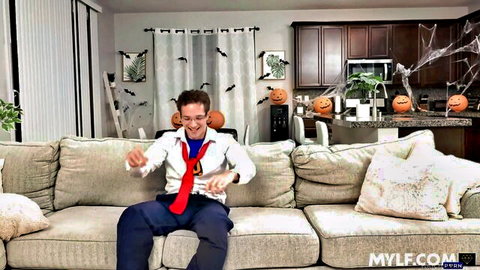 Excited man in white shirt red tie holds game controller on Halloween couch in living room