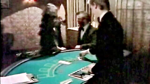 Men in tuxedos dealing cards at green poker table in dimly lit casino room