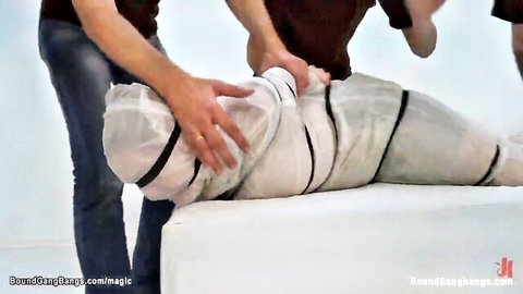 Three men wrapping sexy babe in tight white mummification tape for intense BDSM bondage