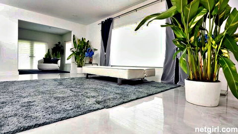 Empty luxurious modern bedroom with white daybed, tropical plants, black curtains and plush gray rug