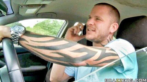 Tattooed muscular man with flame arm tats driving car while talking on phone