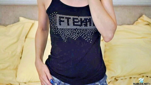 Blonde babe in sparkly black tank top showing cleavage and tight jeans posing on bed