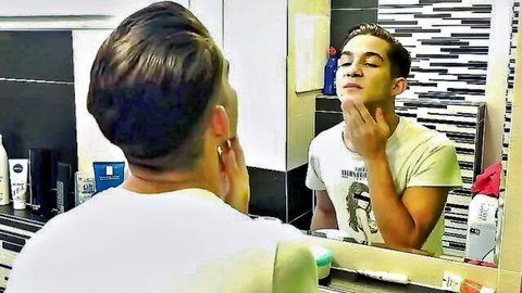 Handsome mixed-race guy in white t-shirt touching face in bathroom mirror