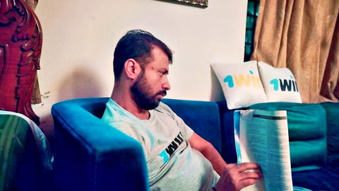 Bearded Indian desi man in gray t-shirt reading newspaper