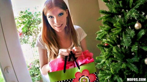 Smiling redhead holding pink-ribboned Christmas gift bag by tree