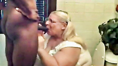 Mature blonde woman in white dress giving blowjob to black man