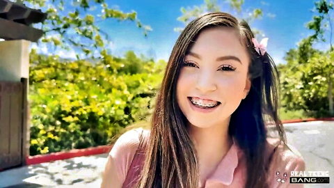 Cute Asian teen Amber Angel with braces smiling outdoors in pink top