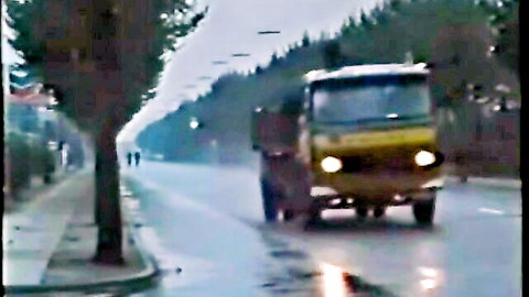 Vintage yellow dump truck on misty urban road with trees and streetlights