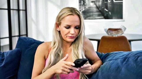 Sexy blonde in tight pink top teasing cleavage while texting on couch