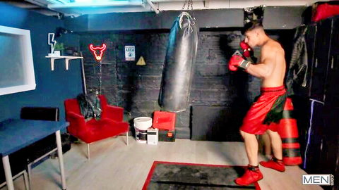 Athletic shirtless boxer in red shorts and gloves poses in steamy gym