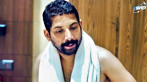 Shirtless bearded Indian man in white towel smirking in steamy bathroom