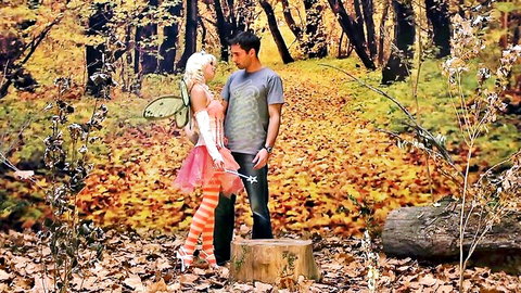 Sexy blonde fairy in skimpy pink tutu and striped stockings poses with handsome guy in autumn forest