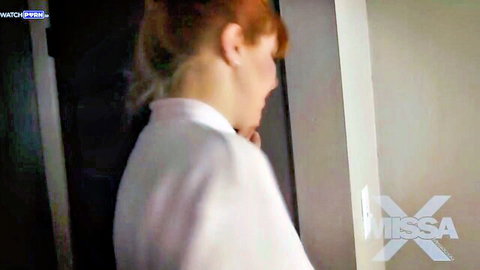 Redhead woman in white shirt stands sideways in elevator with ponytail
