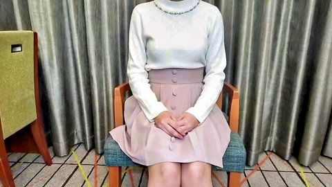 Kinky Asian babe in white turtleneck and pink pleated skirt with uneasy expression