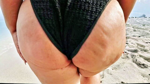 Thick woman's huge juicy ass cheeks spilling out of tiny black thong bikini on beach