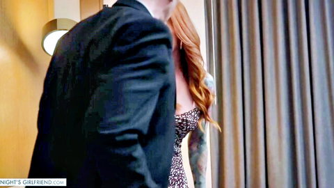 Busty redhead MILF in low-cut dress shows deep cleavage to suited man in hotel room