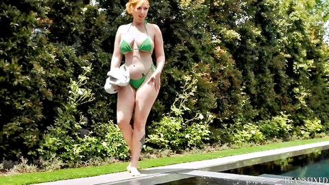 Redhead babe in skimpy green bikini struts poolside with medium tits spilling out