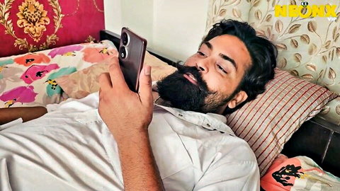 Bearded Desi hubby relaxing on bed with phone, teasing adult fun