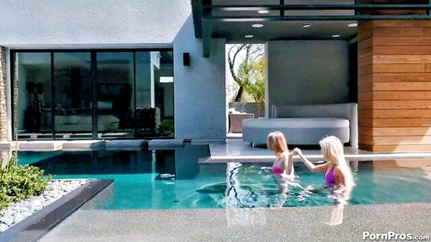 Two busty blondes in tiny pink bikinis playfully splashing in luxury outdoor pool