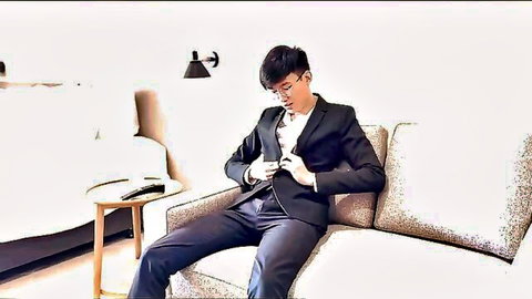 Asian man with glasses in black suit sitting on couch holding phone